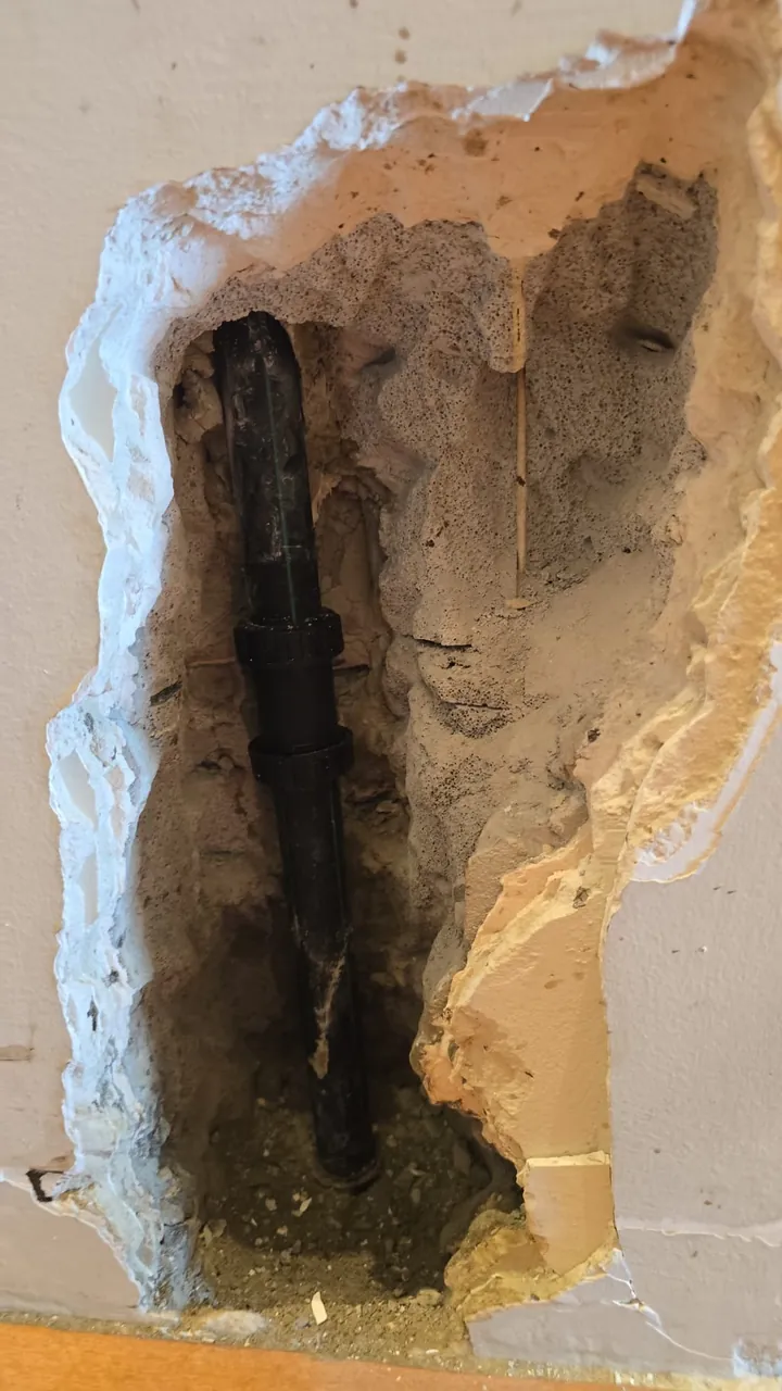 קיר שנפתח וחושף צינור מים מחליד שדלף בתוך הקיר