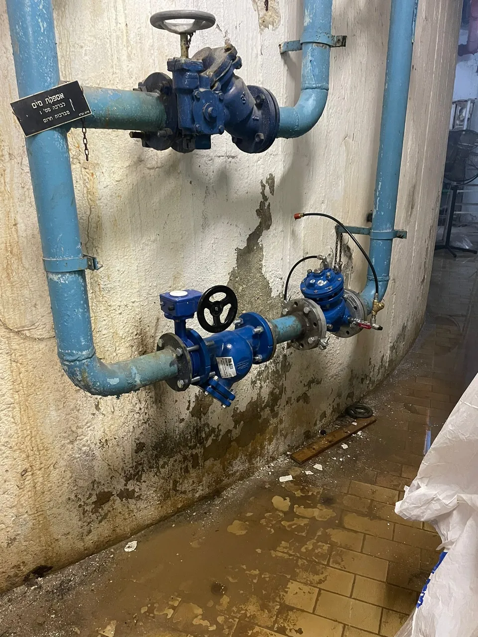 מערך מגופים ומד מים ראשי על קיר במבנה מוסדי