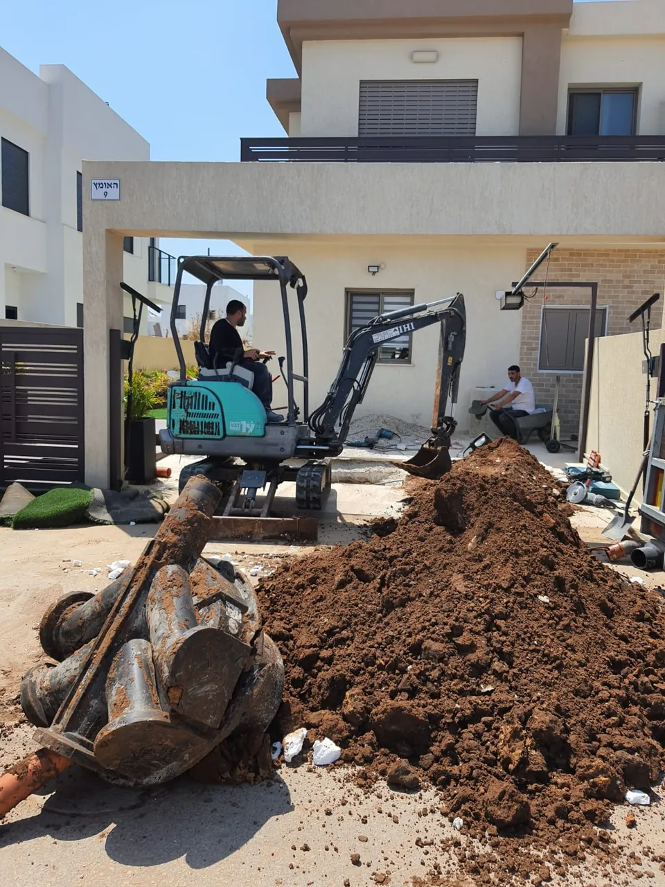 מיני מחפרון עובד בחניה של בית פרטי בלי לפרק את השער