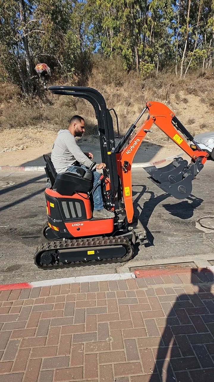 מפעיל מיני מחפרון בעבודה על משטח מרוצף בחצר בניין