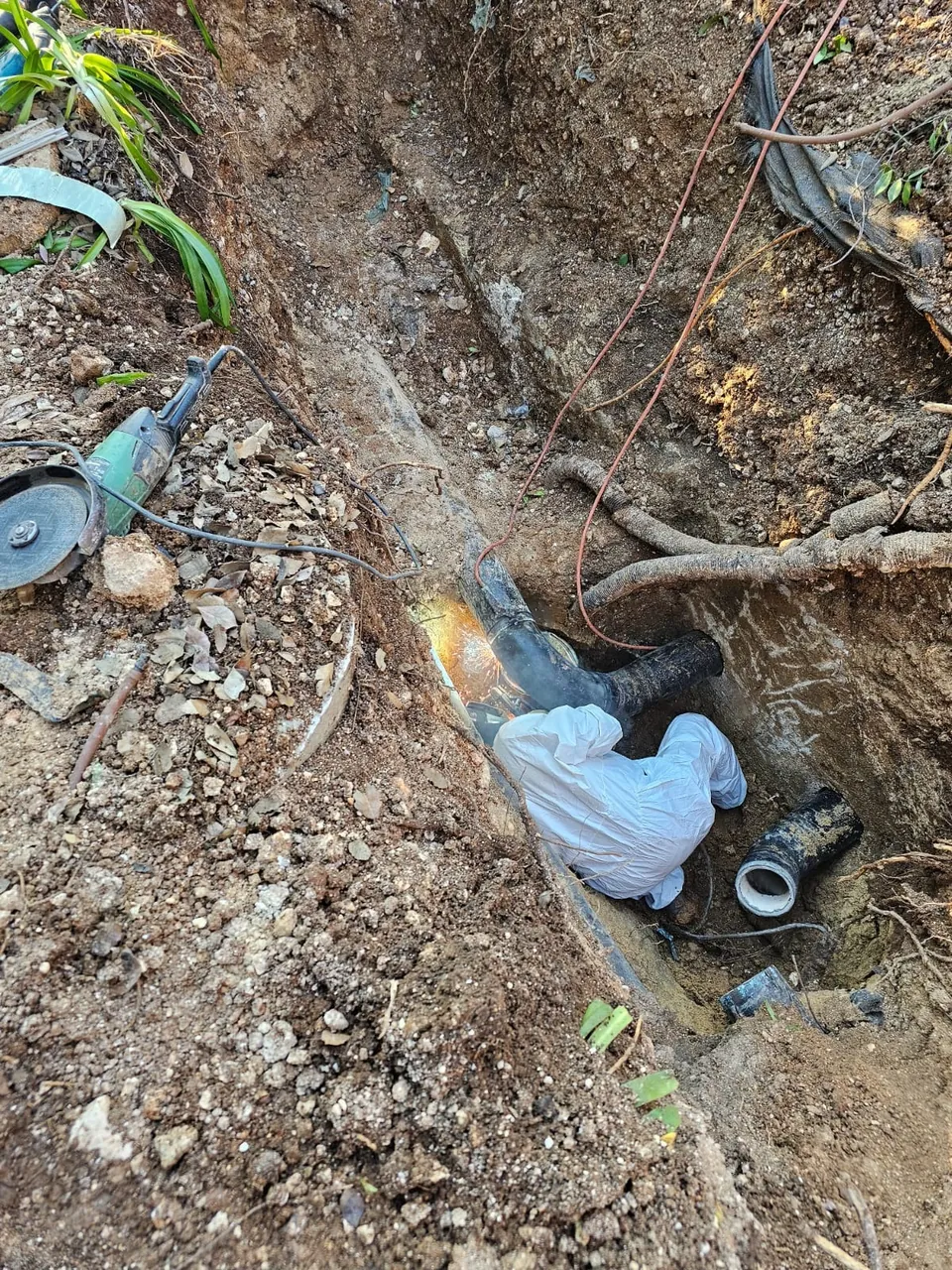 תיקון צנרת בתעלה פתוחה בין שורשי עץ שפגעו בקו
