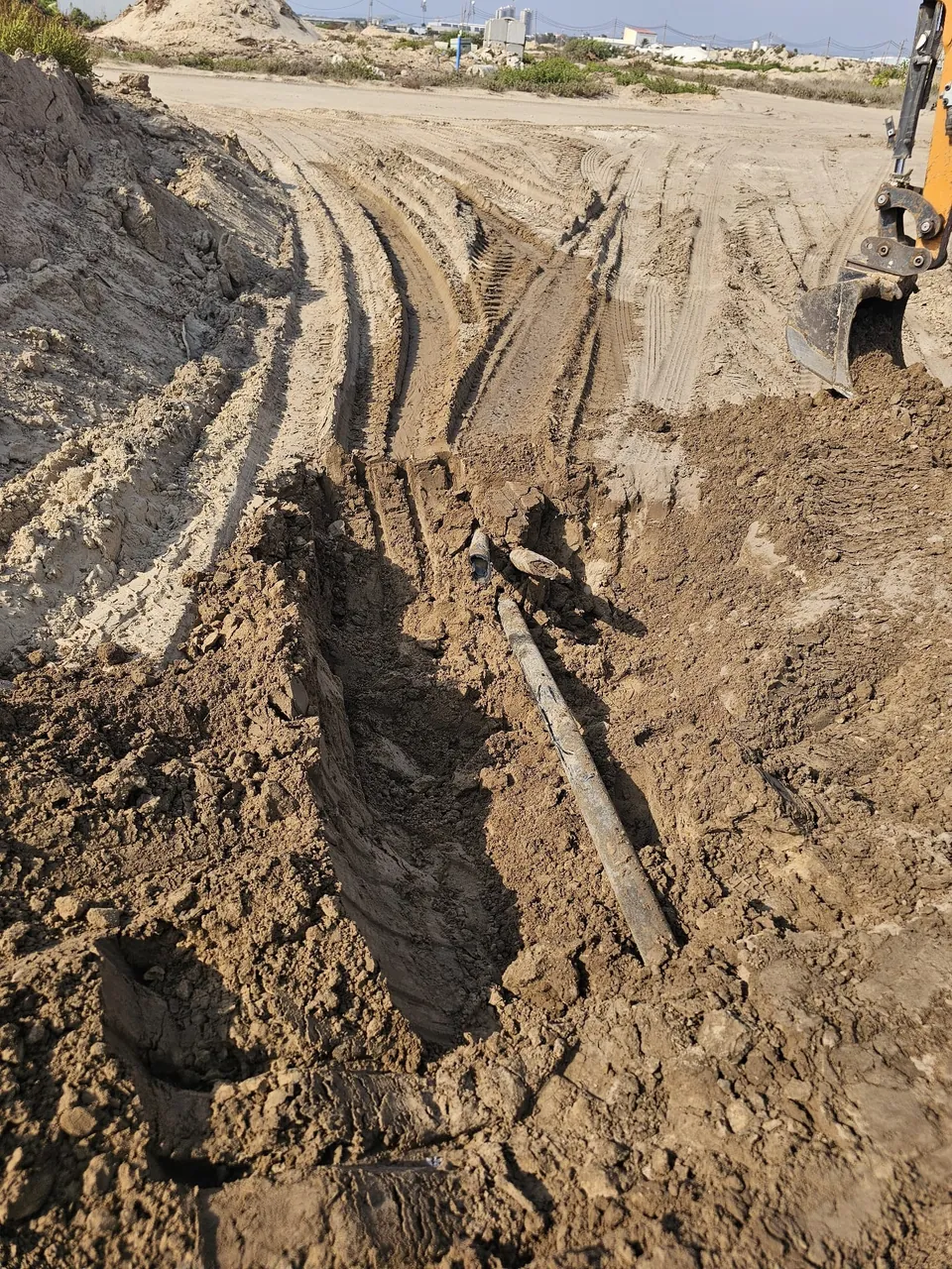 תעלה ארוכה להנחת קו ביוב בשטח חולי עם מחפרון ברקע