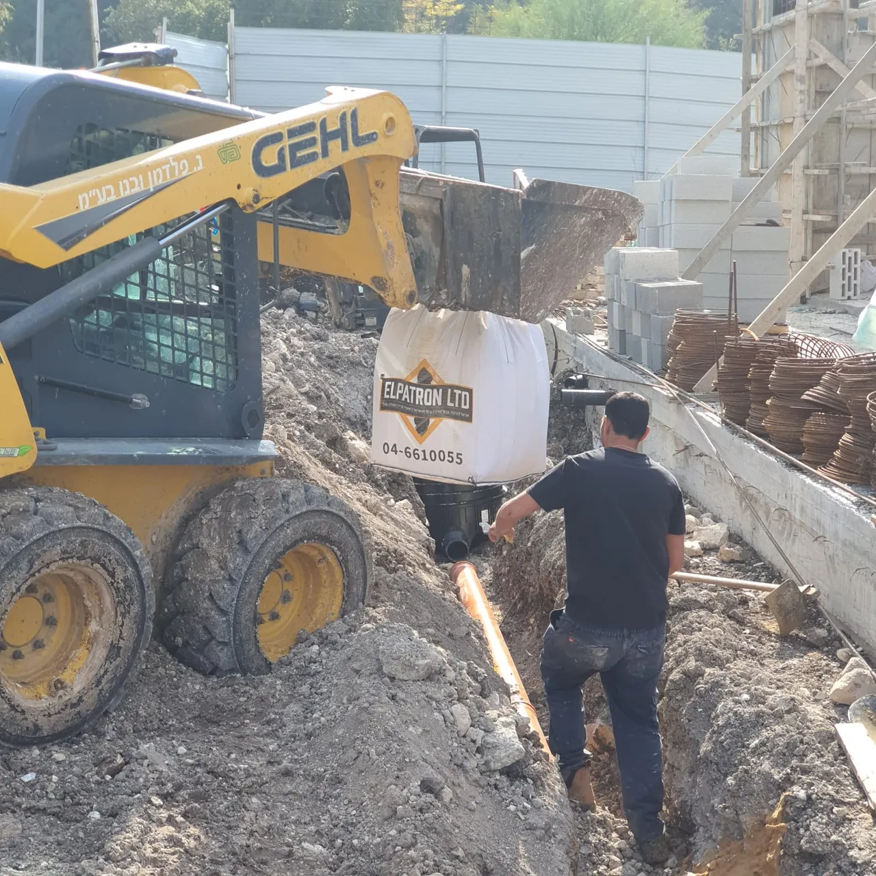 מיני מעמיס ועובד מניחים צינור בתעלה באתר בנייה