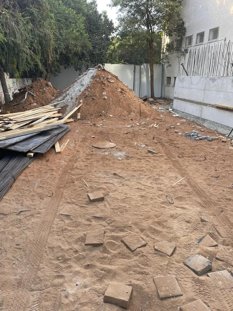 עבודות חפירה בחצר פנימית של מבנה — ערימת עפר וגישה צרה בין הבניין לגדר